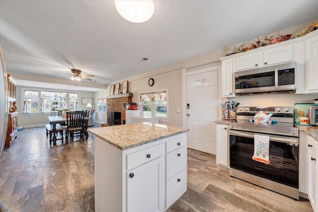 kitchen featuring appliances with stainless steel finishes, white cabinets, a center island, light stone counters, and a brick fireplace