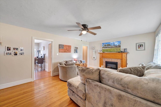 living room with ceiling fan, a textured ceiling, a brick fireplace, and light wood-type flooring