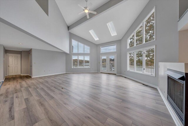 unfurnished living room featuring a skylight, light hardwood / wood-style flooring, high vaulted ceiling, and ceiling fan