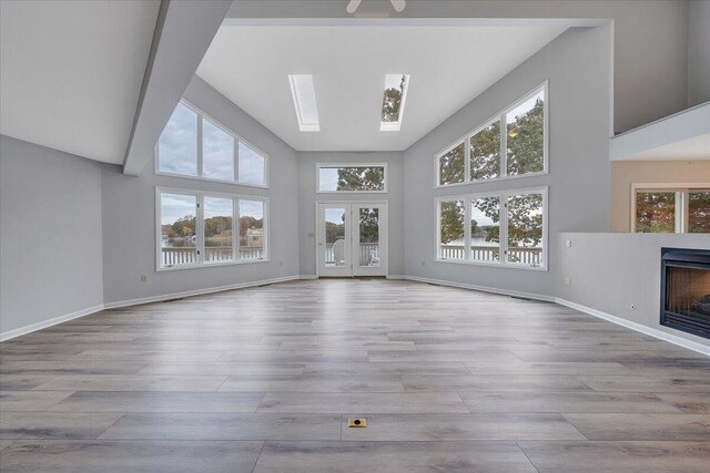 unfurnished living room with a skylight, a wealth of natural light, light hardwood / wood-style floors, and a high ceiling