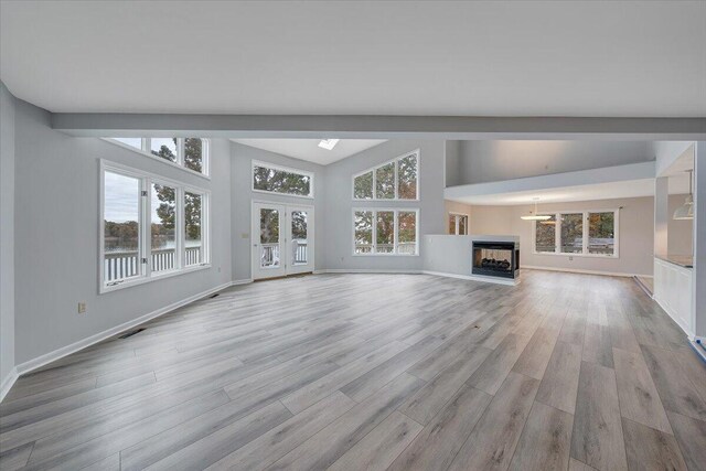 unfurnished living room with vaulted ceiling, a multi sided fireplace, light hardwood / wood-style floors, and french doors