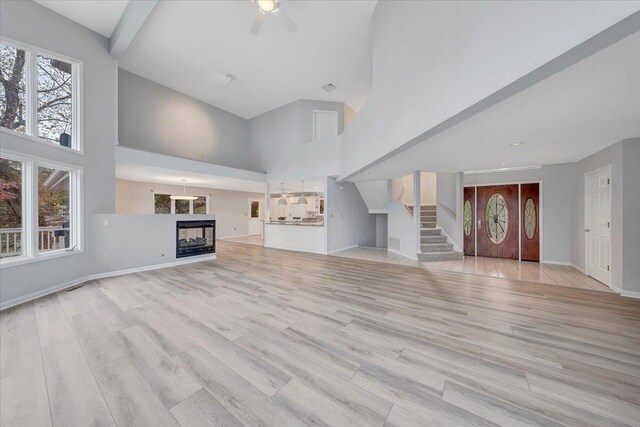 unfurnished living room with a multi sided fireplace, a high ceiling, and light wood-type flooring