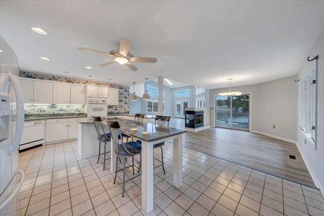 kitchen with a breakfast bar area, white cabinetry, light tile patterned floors, pendant lighting, and white appliances