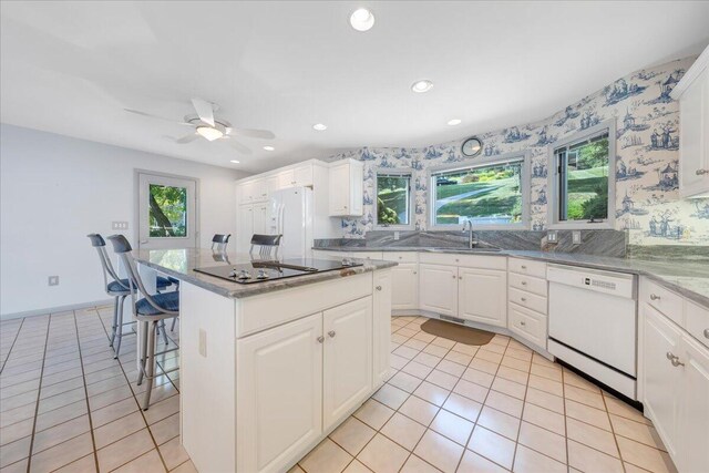 kitchen featuring white appliances, a breakfast bar area, a center island, and white cabinets