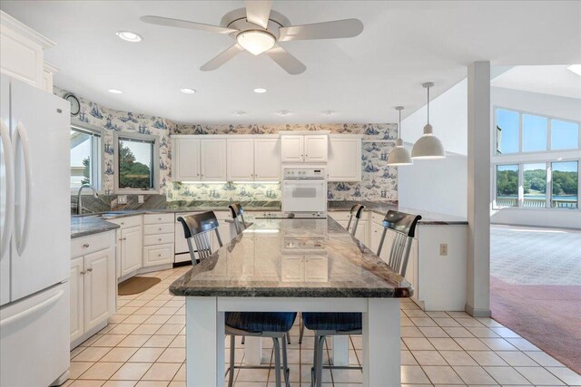 kitchen with a large island, pendant lighting, white appliances, a kitchen breakfast bar, and white cabinets