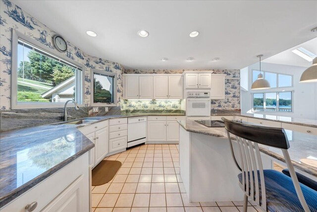 kitchen featuring sink, dishwasher, hanging light fixtures, white cabinets, and dark stone counters