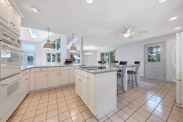 kitchen featuring a kitchen island, white cabinetry, hanging light fixtures, light stone countertops, and white appliances