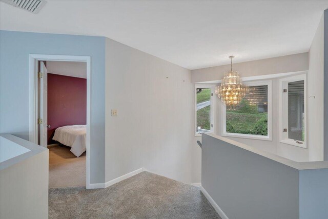 corridor with light carpet and a notable chandelier