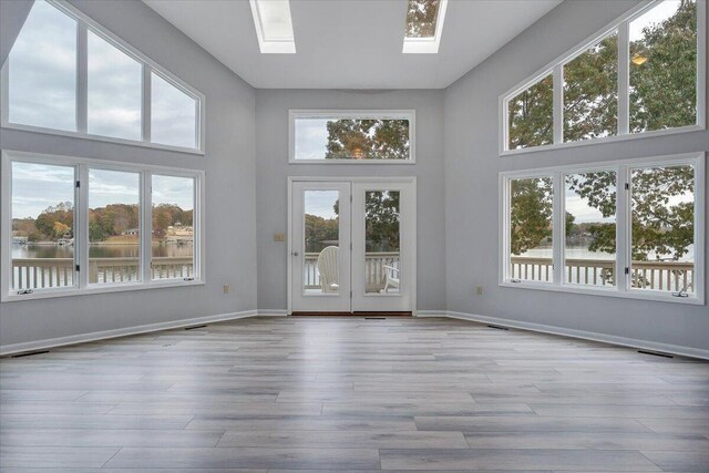 unfurnished sunroom with a skylight, french doors, a healthy amount of sunlight, and a water view