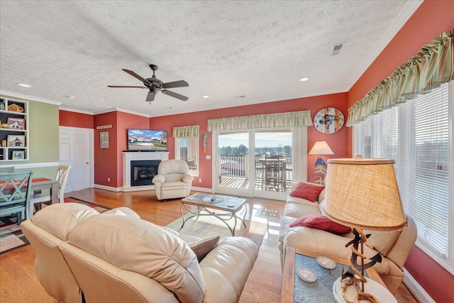 living room featuring ceiling fan, ornamental molding, a textured ceiling, and light wood-type flooring