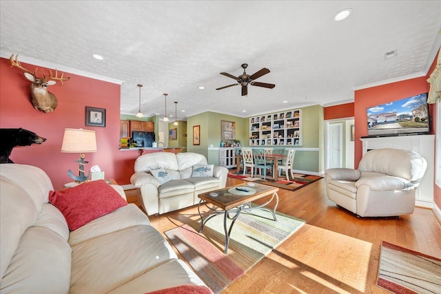 living room featuring ceiling fan, light hardwood / wood-style flooring, ornamental molding, and a textured ceiling