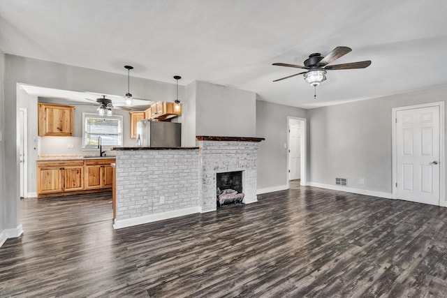 unfurnished living room with dark wood-type flooring, ceiling fan, sink, and a brick fireplace