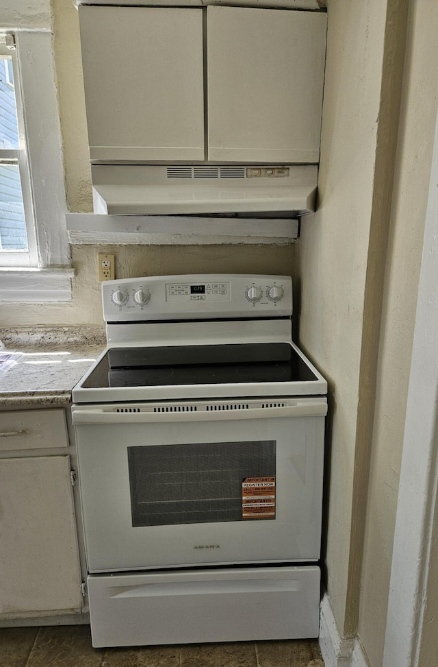 kitchen view of white electric range oven, under cabinet range hood, light countertops, and white cabinetry