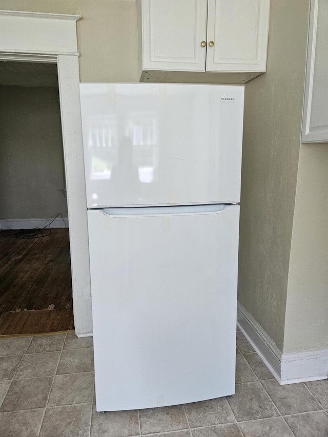 kitchen view of freestanding refrigerator, white cabinets, and baseboards