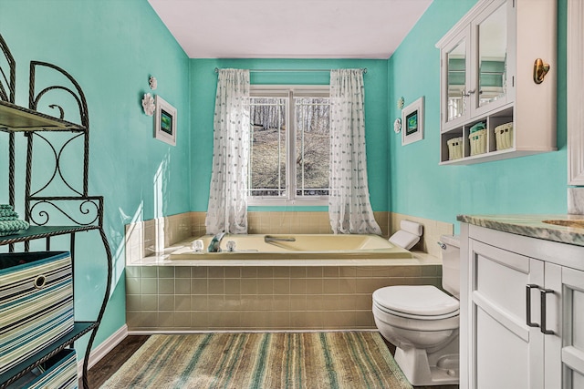 bathroom featuring vanity, tiled bath, and toilet