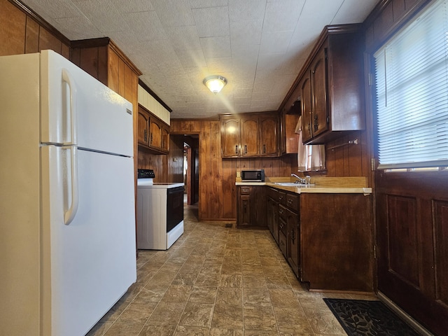 kitchen featuring sink, white appliances, wooden walls, and dark brown cabinets