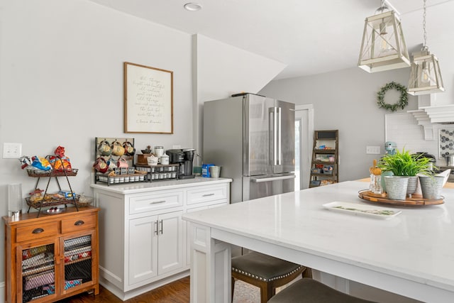 kitchen featuring pendant lighting, stainless steel refrigerator, white cabinetry, tasteful backsplash, and a kitchen bar