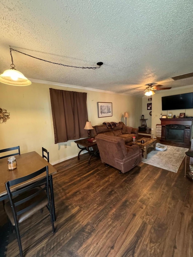 living room featuring dark wood-type flooring, ceiling fan, crown molding, and a textured ceiling