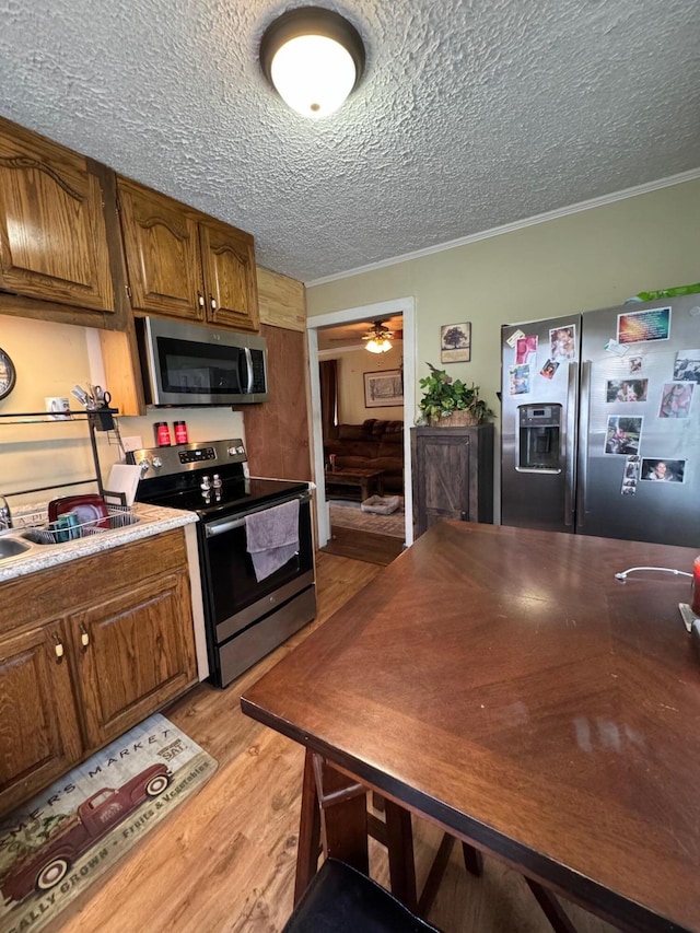 kitchen featuring ornamental molding, ceiling fan, light hardwood / wood-style floors, stainless steel appliances, and a textured ceiling