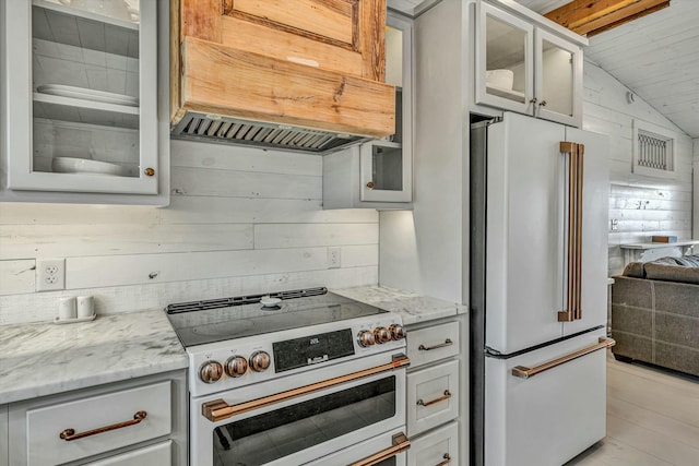 kitchen with vaulted ceiling, wood walls, high quality appliances, custom exhaust hood, and light stone counters