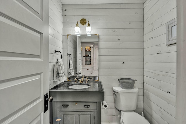 bathroom with vanity, wooden walls, and toilet