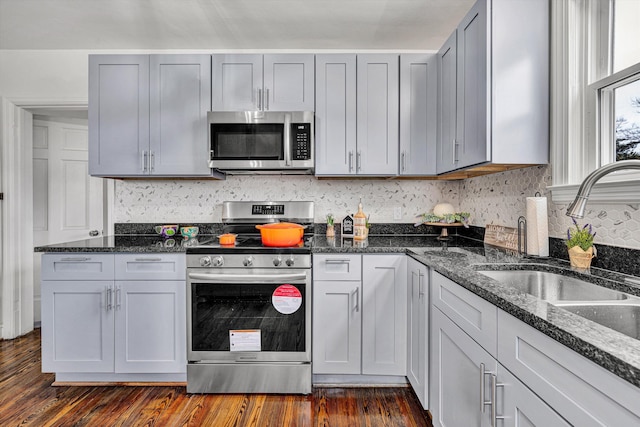 kitchen featuring stainless steel appliances, dark hardwood / wood-style floors, sink, and dark stone counters