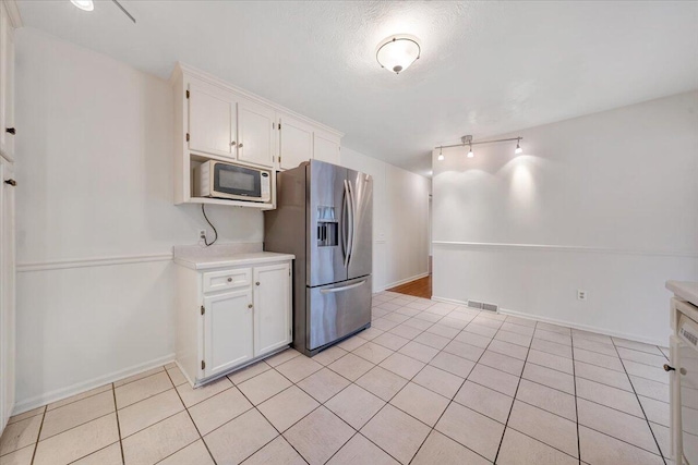 kitchen featuring a textured ceiling, stainless steel fridge, white cabinets, and light tile patterned flooring