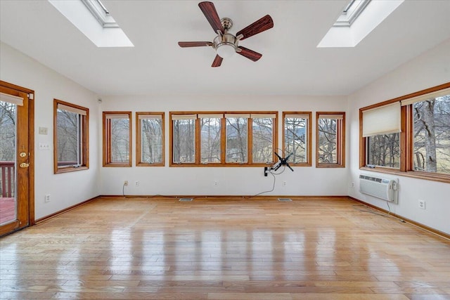 unfurnished sunroom with a wall mounted AC, vaulted ceiling with skylight, and ceiling fan