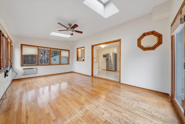 unfurnished living room with ceiling fan, a skylight, and light hardwood / wood-style flooring