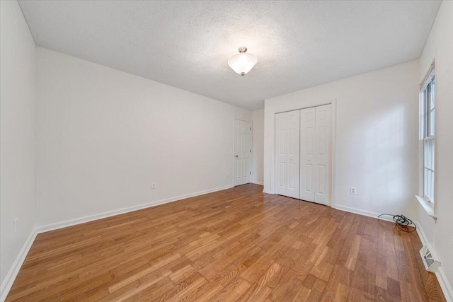 unfurnished bedroom with multiple windows, a textured ceiling, light wood-type flooring, and a closet