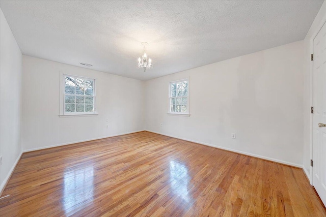 unfurnished room featuring an inviting chandelier, a wealth of natural light, and light wood-type flooring