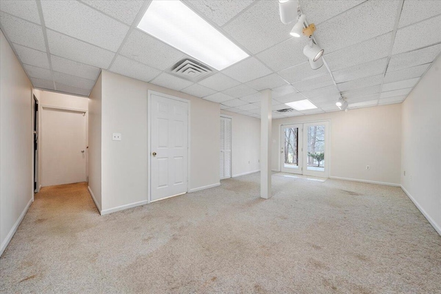 basement with a paneled ceiling, light colored carpet, french doors, and track lighting