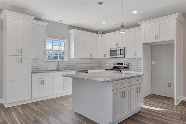 kitchen with sink, white cabinetry, stainless steel appliances, a center island, and light stone counters