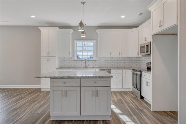 kitchen featuring sink, white cabinetry, a center island, appliances with stainless steel finishes, and light stone countertops