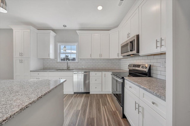 kitchen with white cabinetry, sink, hanging light fixtures, light stone counters, and stainless steel appliances