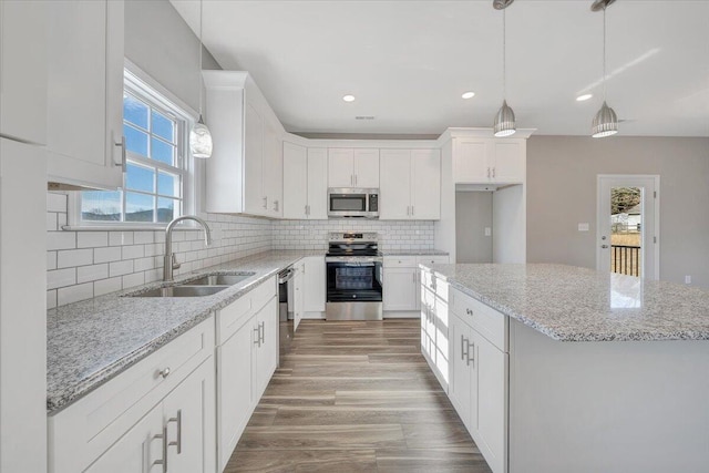 kitchen with sink, white cabinetry, a center island, stainless steel appliances, and light stone countertops