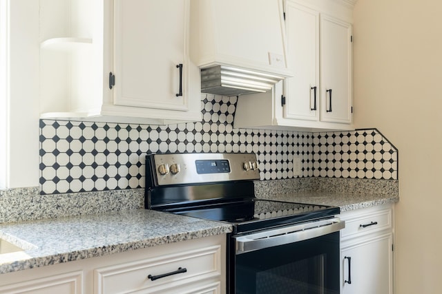 kitchen with tasteful backsplash, white cabinetry, electric range, light stone counters, and custom range hood