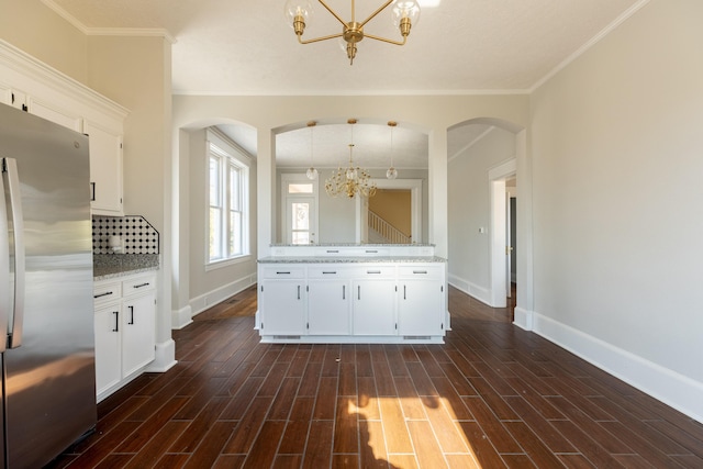 kitchen featuring pendant lighting, stainless steel fridge, light stone countertops, white cabinets, and a chandelier