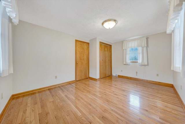 unfurnished bedroom with multiple closets, a textured ceiling, and light hardwood / wood-style floors