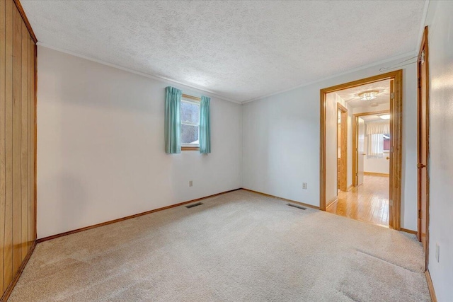 empty room with ornamental molding, light colored carpet, and a textured ceiling