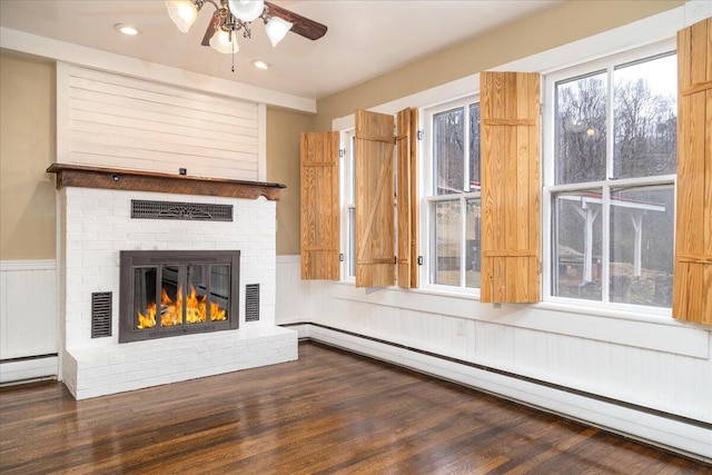 unfurnished living room featuring a baseboard radiator, dark wood-type flooring, ceiling fan, and a fireplace