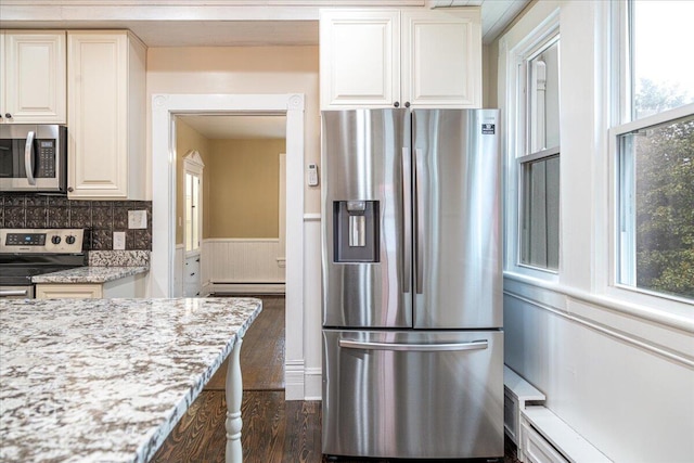 kitchen featuring light stone countertops, appliances with stainless steel finishes, a baseboard heating unit, and a wealth of natural light