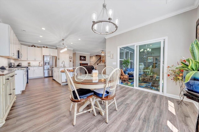 dining area featuring crown molding, sink, ceiling fan with notable chandelier, and light hardwood / wood-style flooring