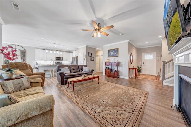 living room with sink, crown molding, ceiling fan, and light wood-type flooring