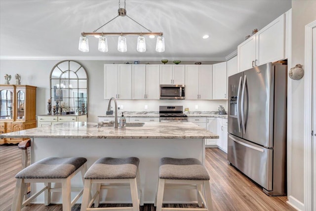 kitchen featuring white cabinetry, light stone counters, ornamental molding, an island with sink, and stainless steel appliances