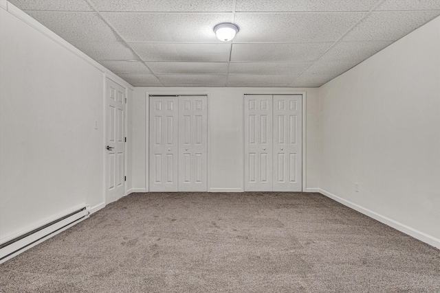 unfurnished bedroom featuring a baseboard heating unit, carpet floors, multiple closets, and a paneled ceiling