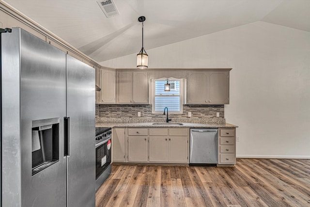 kitchen featuring appliances with stainless steel finishes, lofted ceiling, sink, backsplash, and hardwood / wood-style flooring