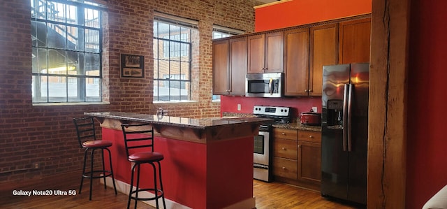 kitchen featuring a kitchen breakfast bar, brick wall, stainless steel appliances, a center island, and dark stone countertops