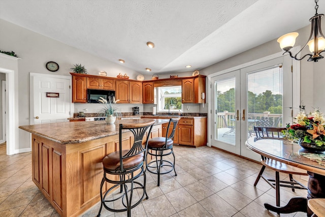 kitchen featuring black microwave, lofted ceiling, hanging light fixtures, french doors, and a center island