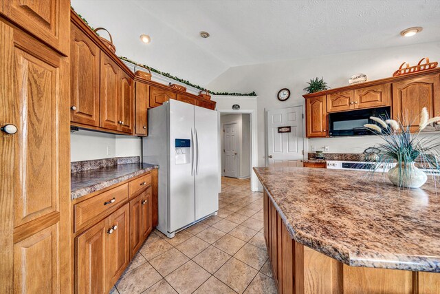 kitchen with stainless steel fridge, brown cabinetry, lofted ceiling, black microwave, and light tile patterned flooring